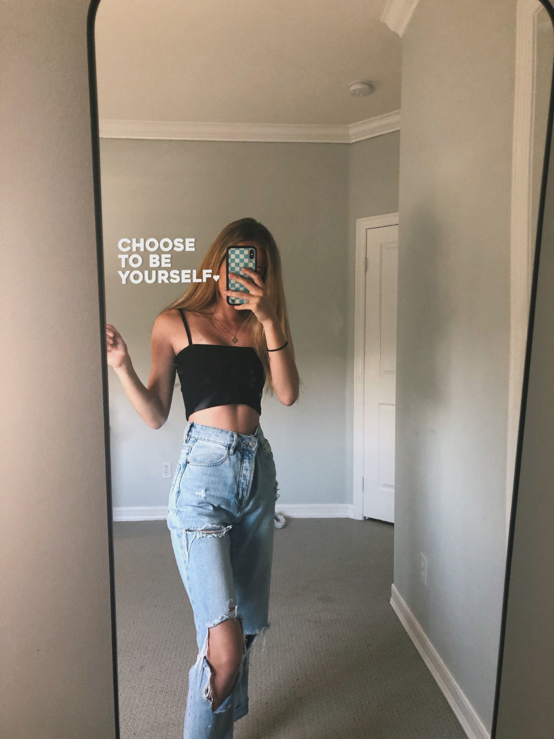 image of woman standing in front of a mirror taking a selfie with the affirmation sticker 'choose to be yourself' in white showing in the foreground
